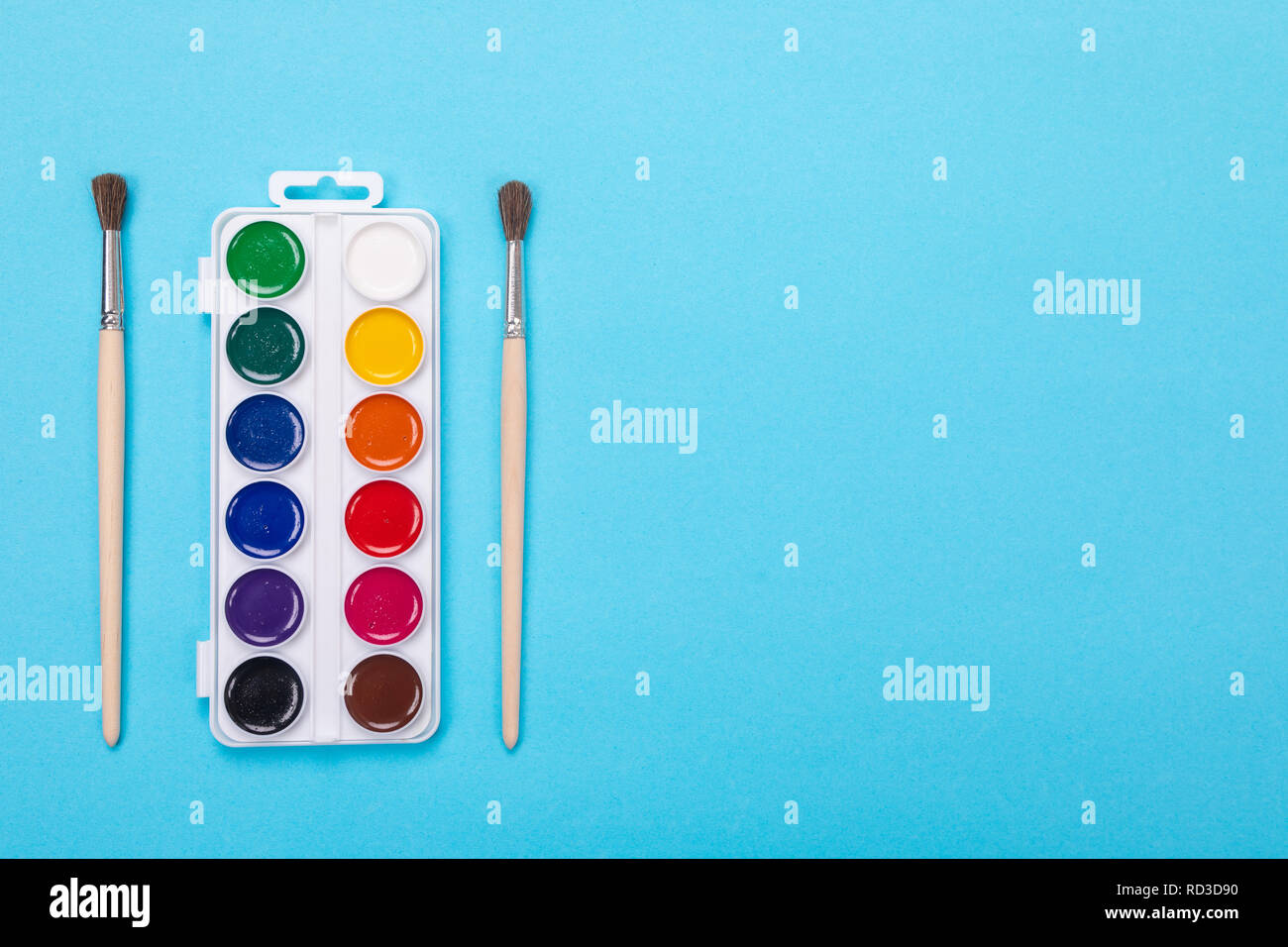 Watercolor paints and brushes in white box, isolated on blue background Stock Photo