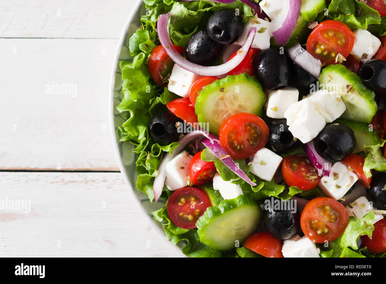 Fresh Greek salad in bowl with black olive,tomato,feta cheese, cucumber and onion on white wooden table. Top view. Stock Photo
