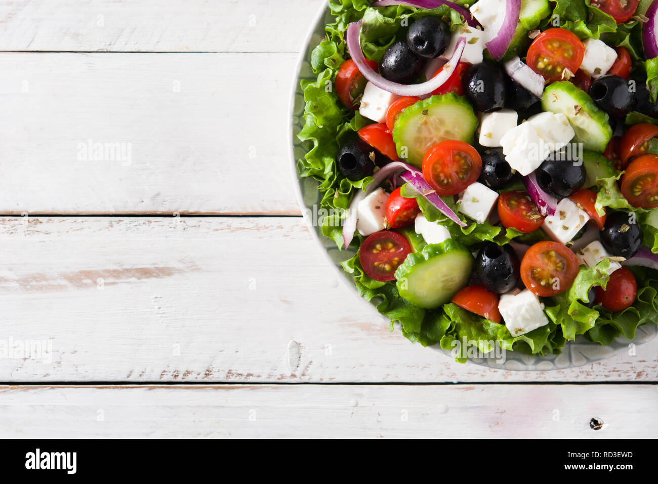 Fresh Greek salad in bowl with black olive,tomato,feta cheese, cucumber and onion on white wooden table. Top view.Copyspace Stock Photo