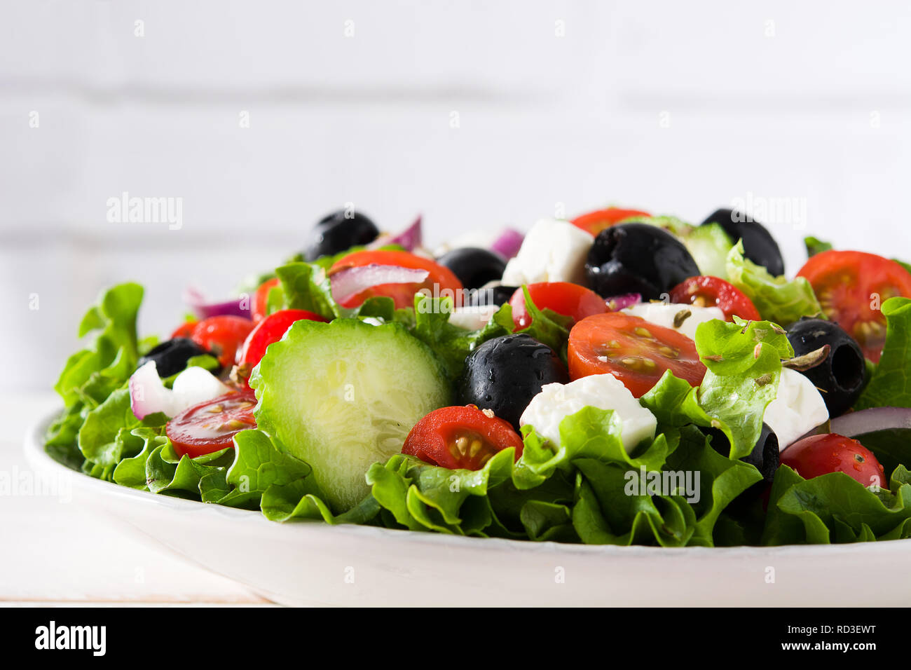 Fresh Greek salad in bowl with black olive,tomato,feta cheese, cucumber and onion on white wooden table. Close up Stock Photo