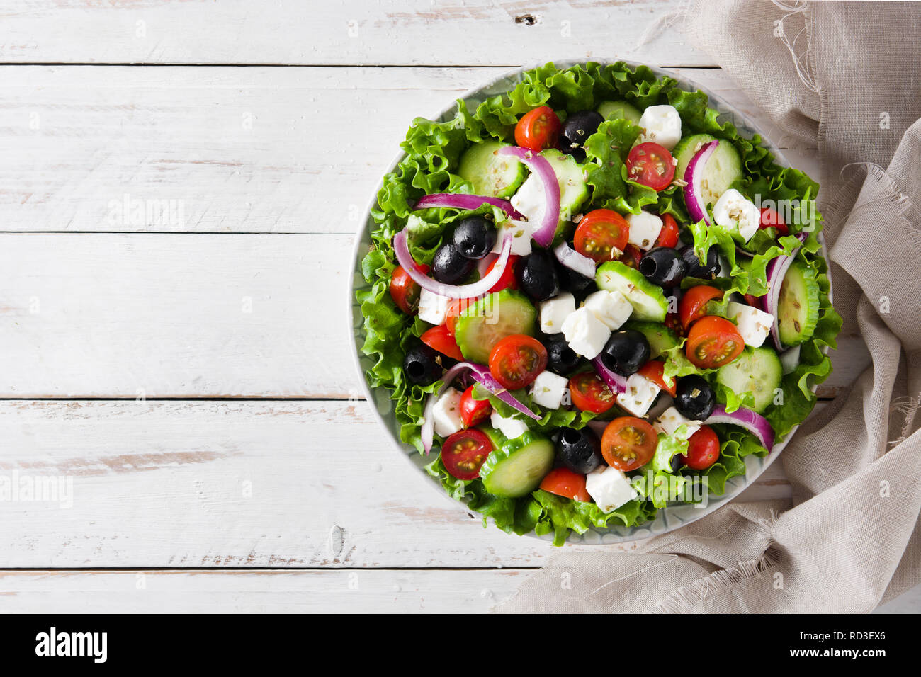 Fresh Greek salad in bowl with black olive,tomato,feta cheese, cucumber and onion on white wooden table. Top view.Copyspace Stock Photo