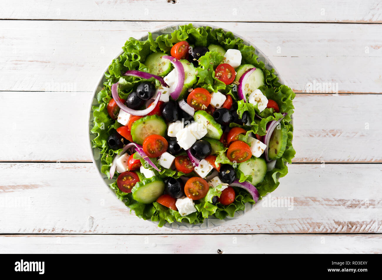 Fresh Greek salad in bowl with black olive,tomato,feta cheese, cucumber and onion on white wooden table. Top view. Stock Photo