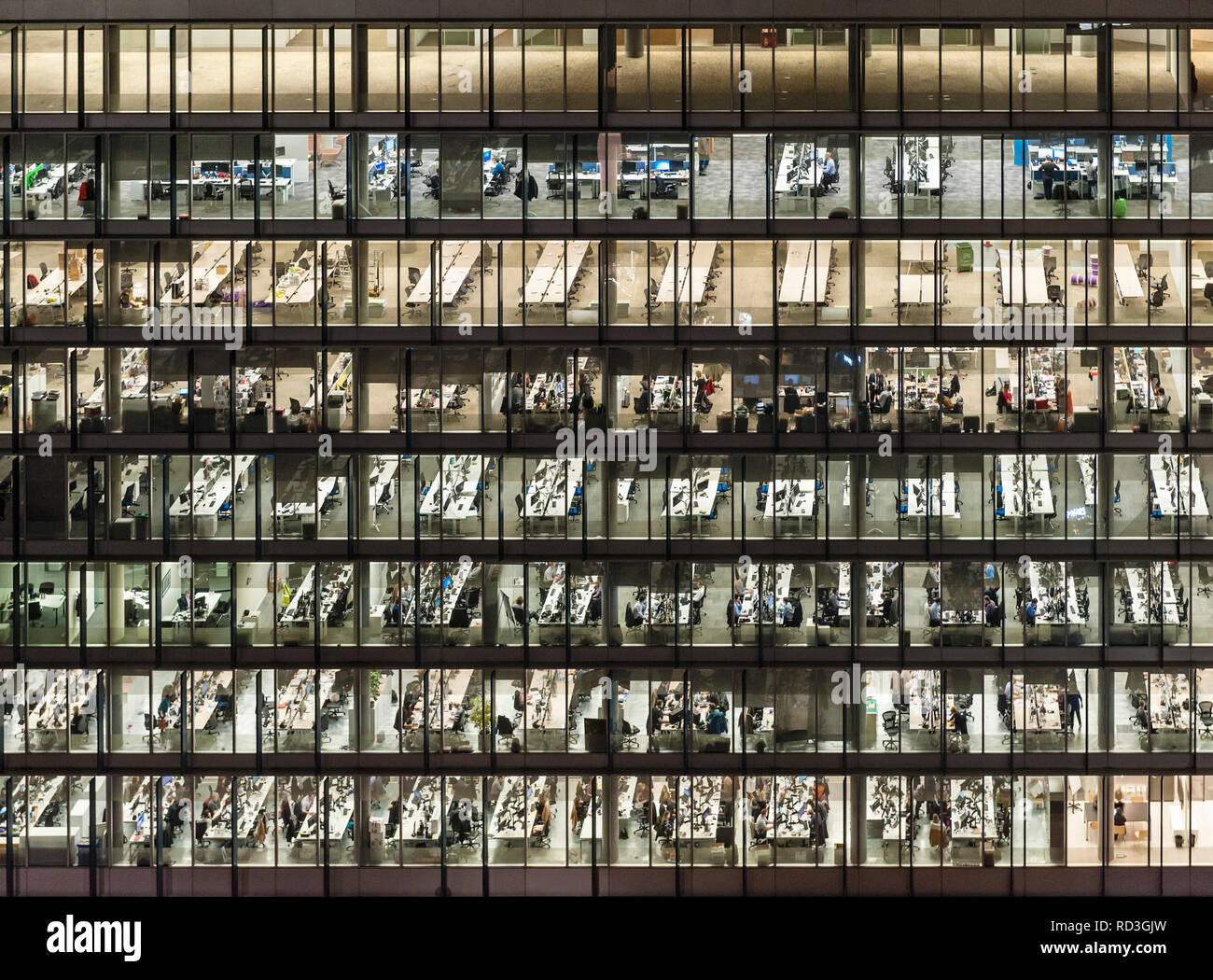 London, UK. Office workers at night, seen through the windows of an office block in the City, London's financial district Stock Photo