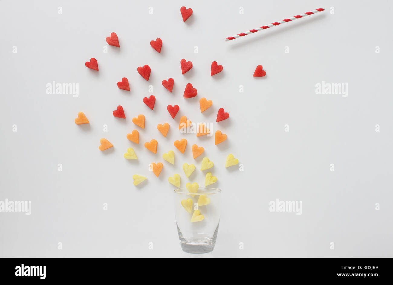 Heart shaped fruit and drinking straw floating out of a glass Stock Photo