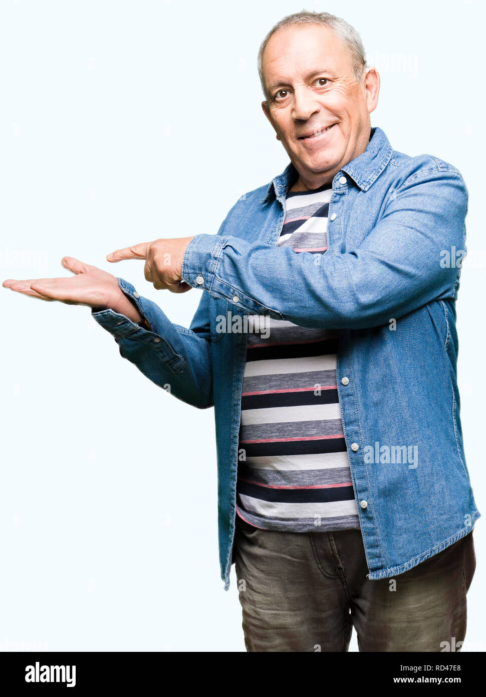 Handsome senior man wearing denim jacket amazed and smiling to the camera while presenting with hand and pointing with finger Stock Photo Alamy