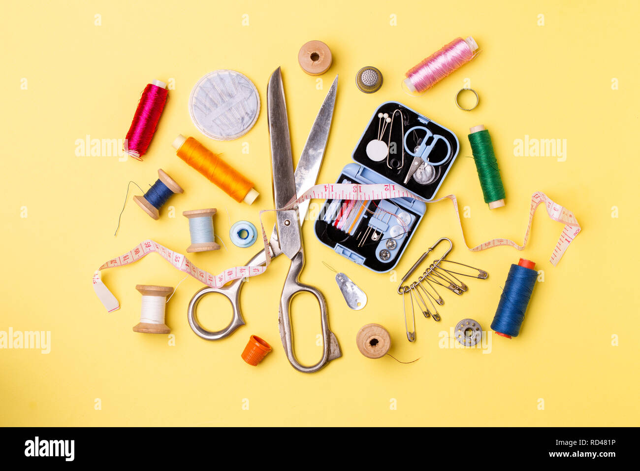 Composition with threads and sewing accessories - scissors, centimeter, pins on yellow background. Stock Photo