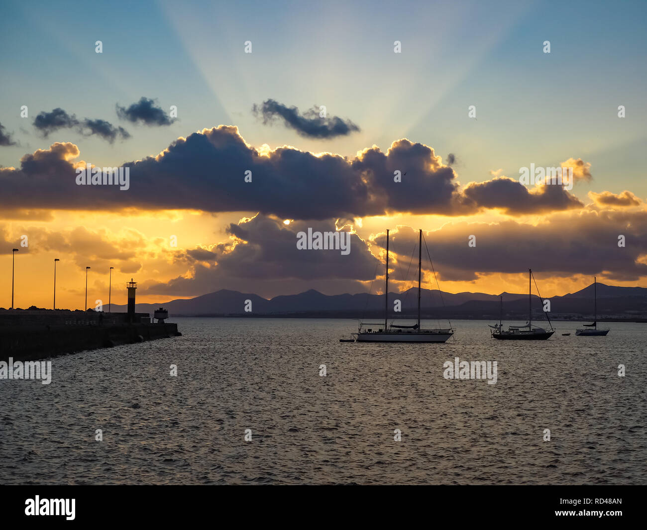 Dramatic sky with upward light rays at sunset over the ocean with peaceful sailing boats at Arrecife, Lanzarote, Canary Islands Stock Photo