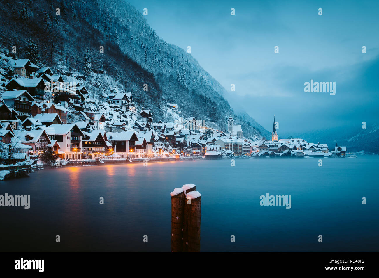 Panorama view of famous Hallstatt lakeside town in the Alps in mystic twilight during blue hour at dawn on a beautiful cold foggy day in winter, Salzk Stock Photo