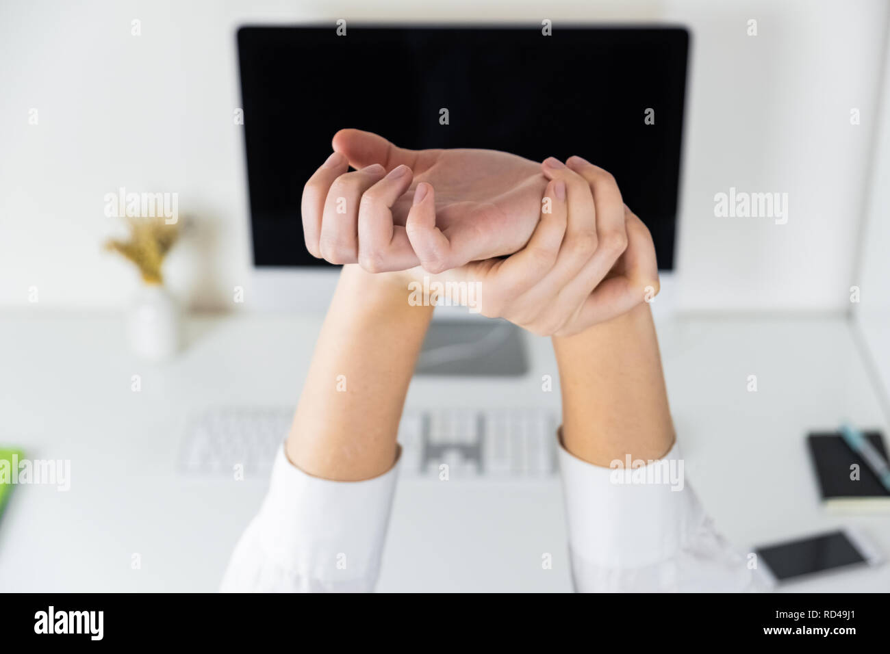Stretching arms in sparse office workplace. Hands of an employee in front of modern desktop, overwork and tiredness concept Stock Photo