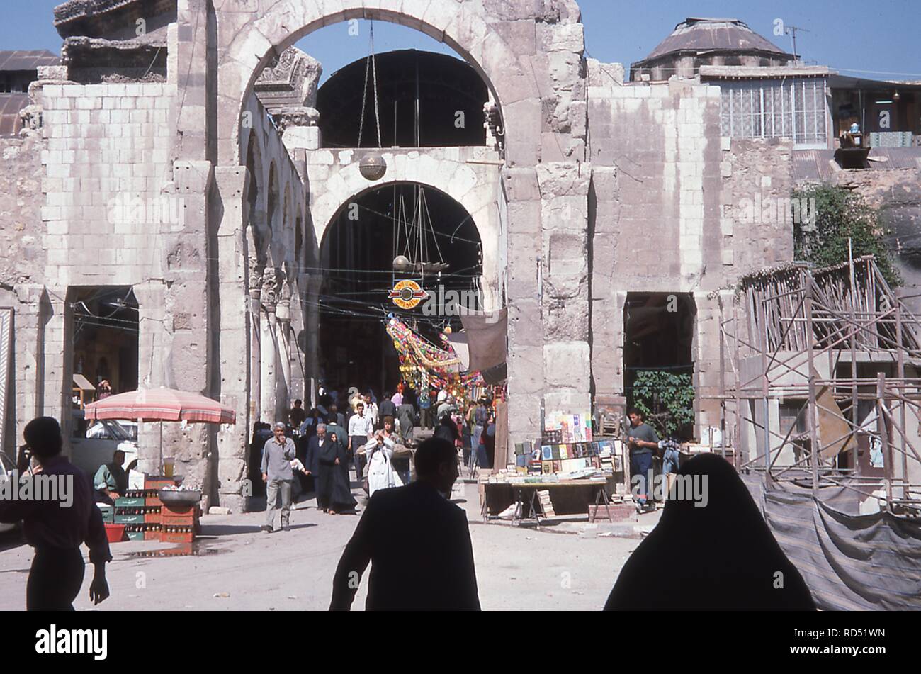 Busy street scene outside the Al-Hamidiyah Souk in the Old City of Damascus, Syria, June, 1994. Men and women walk among the stalls selling books, refreshments, and decorations just outside the entrance. () Stock Photo