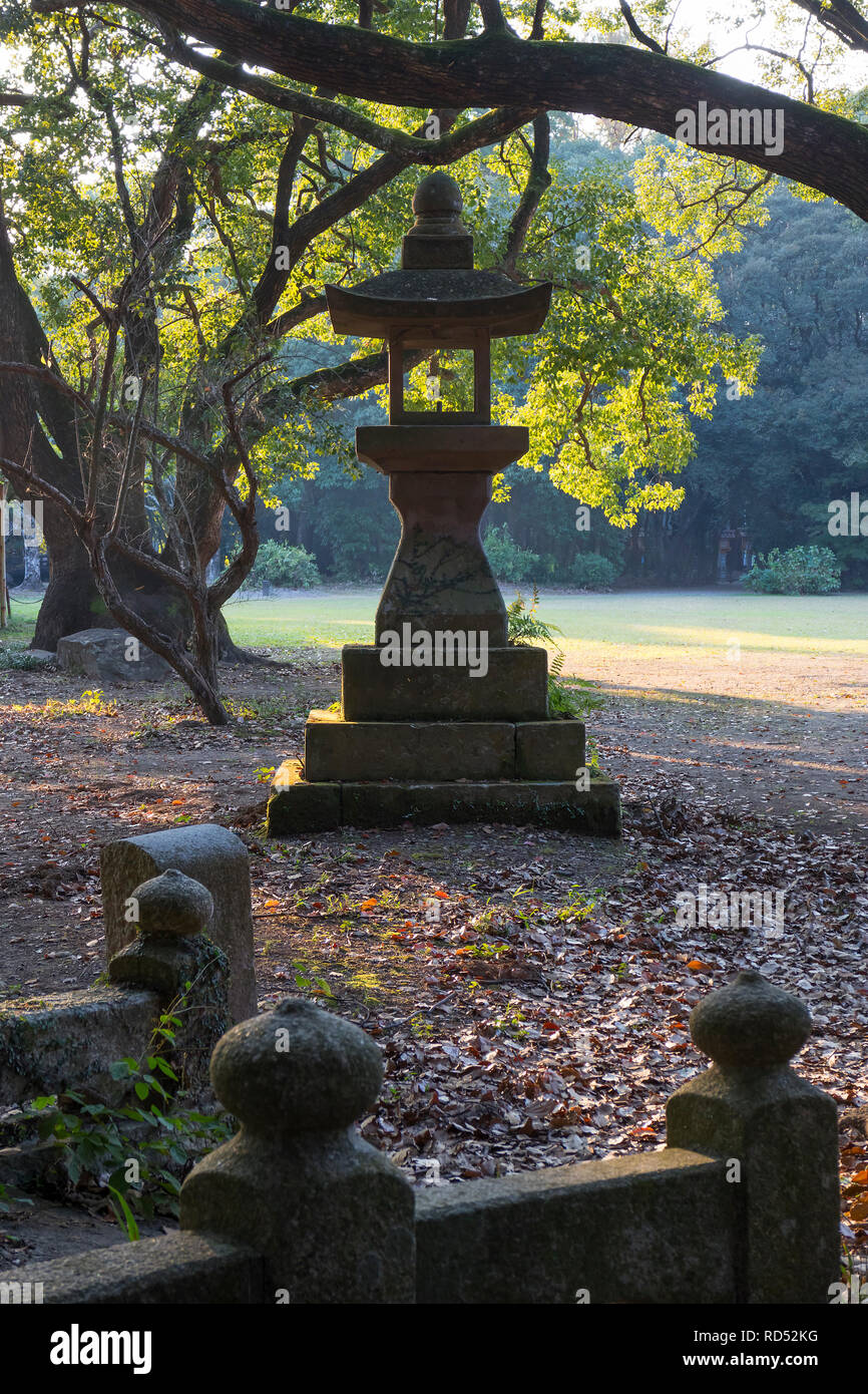 Miyazaki, Japan - November 5, 2018:Old stone lantern at the Miyazaki Jingu shrine grounds in autumn at dusk Stock Photo