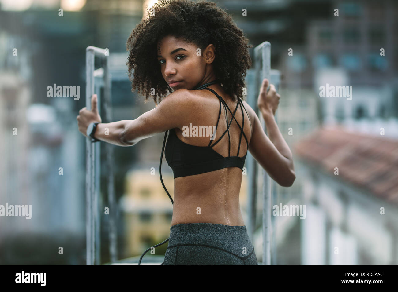 Portrait of an afro american athlete standing holding rooftop staircase. Female athlete doing fitness training standing on rooftop. Stock Photo