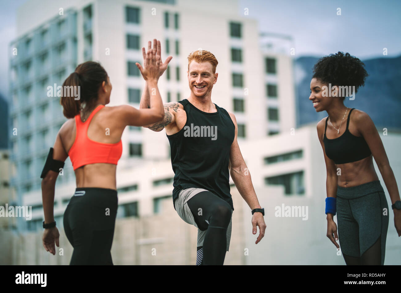 Female athlete giving high five to a man after fitness training standing on rooftop. fitness man and women in cheerful mood giving high five. Stock Photo