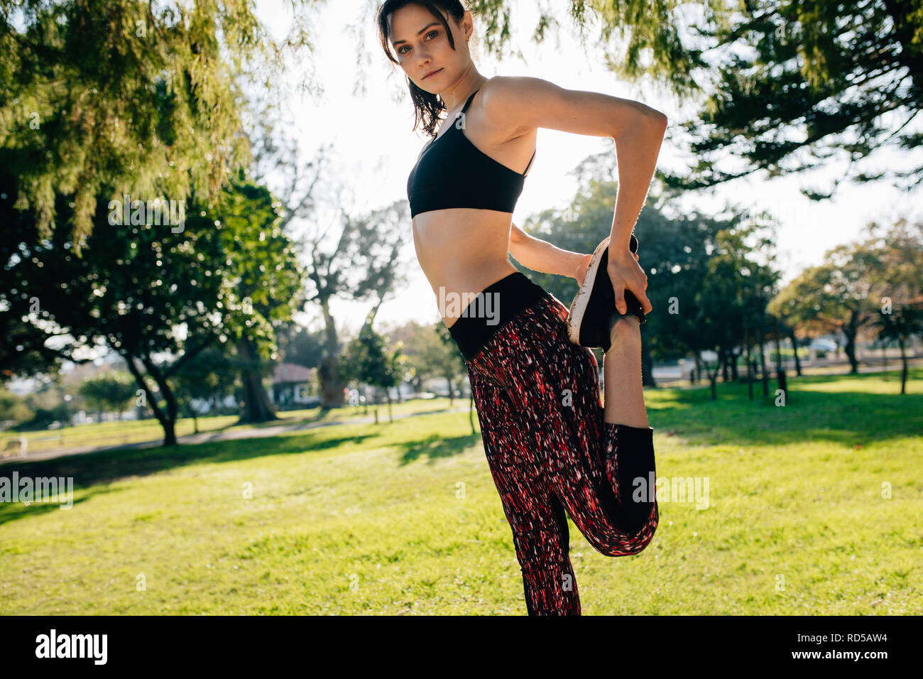 Fit young woman stretching legs and looking at camera.  Caucasian female exercising at the park in morning. Stock Photo