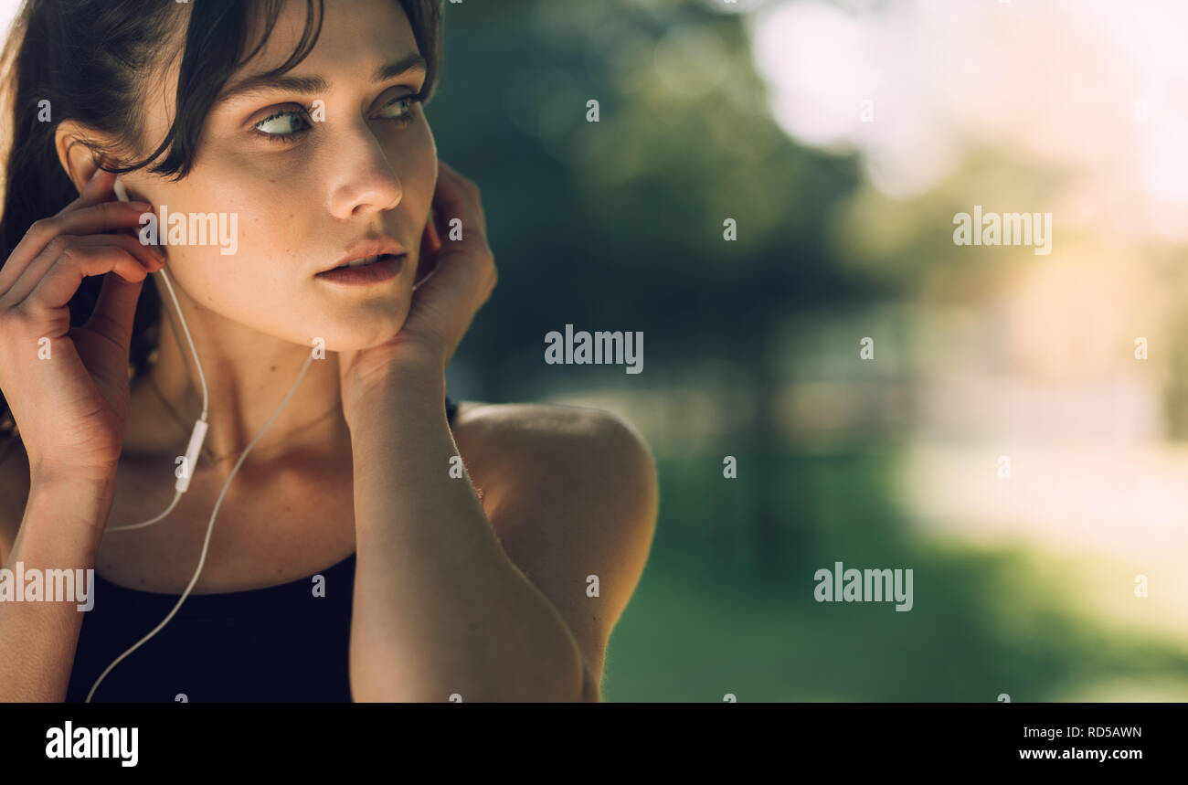 Close up of a fitness woman adjusting her earphones and looking away. Sportswoman with earphones outdoors. Stock Photo