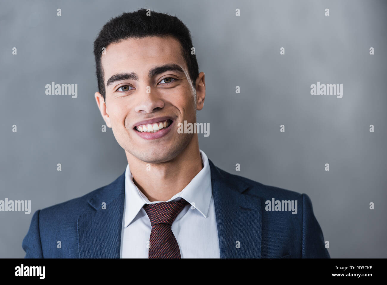 portrait of handsome young businessman smiling at camera on grey Stock ...