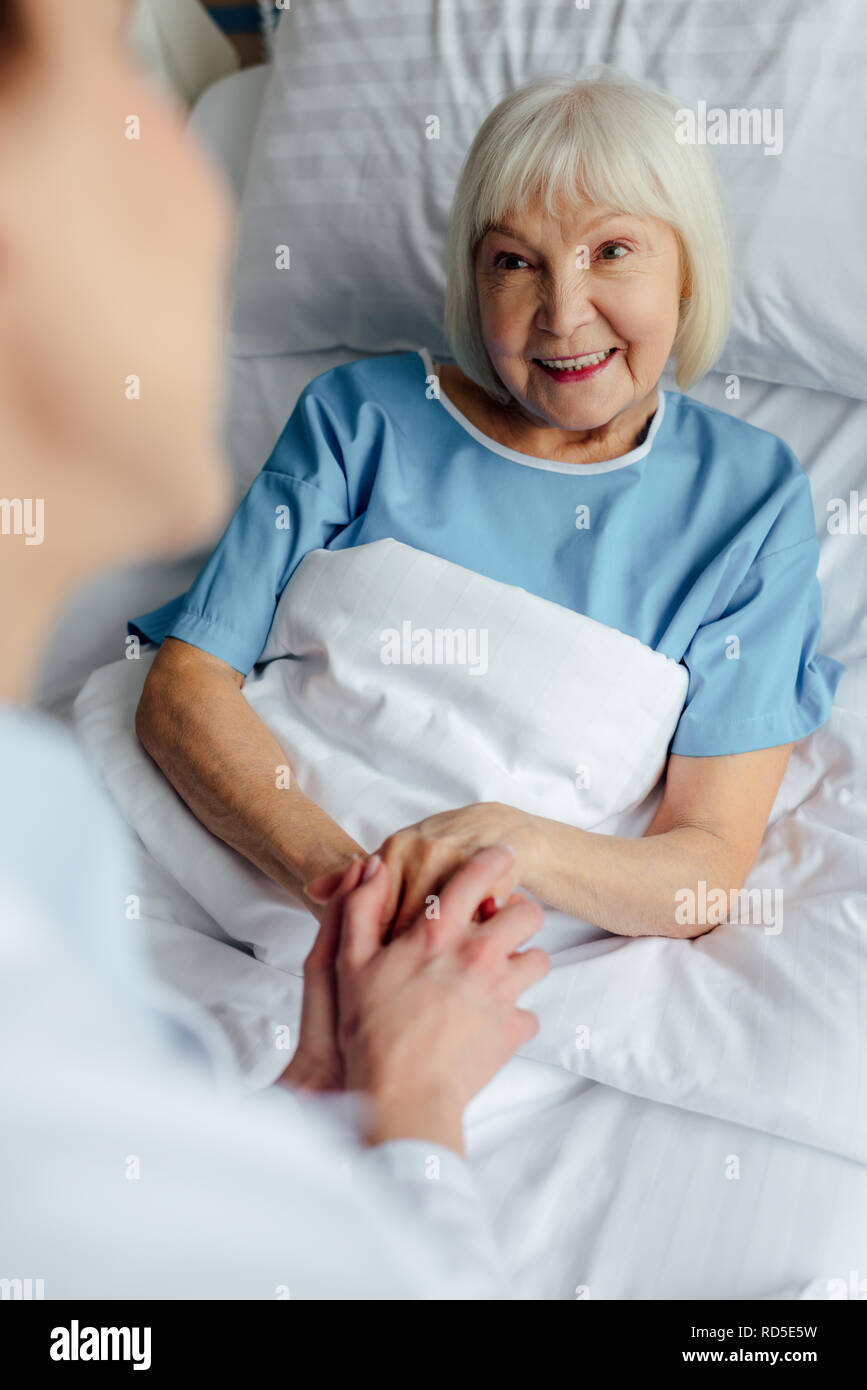 female doctor holding hands with happy senior woman lying in bed in hospital Stock Photo Alamy