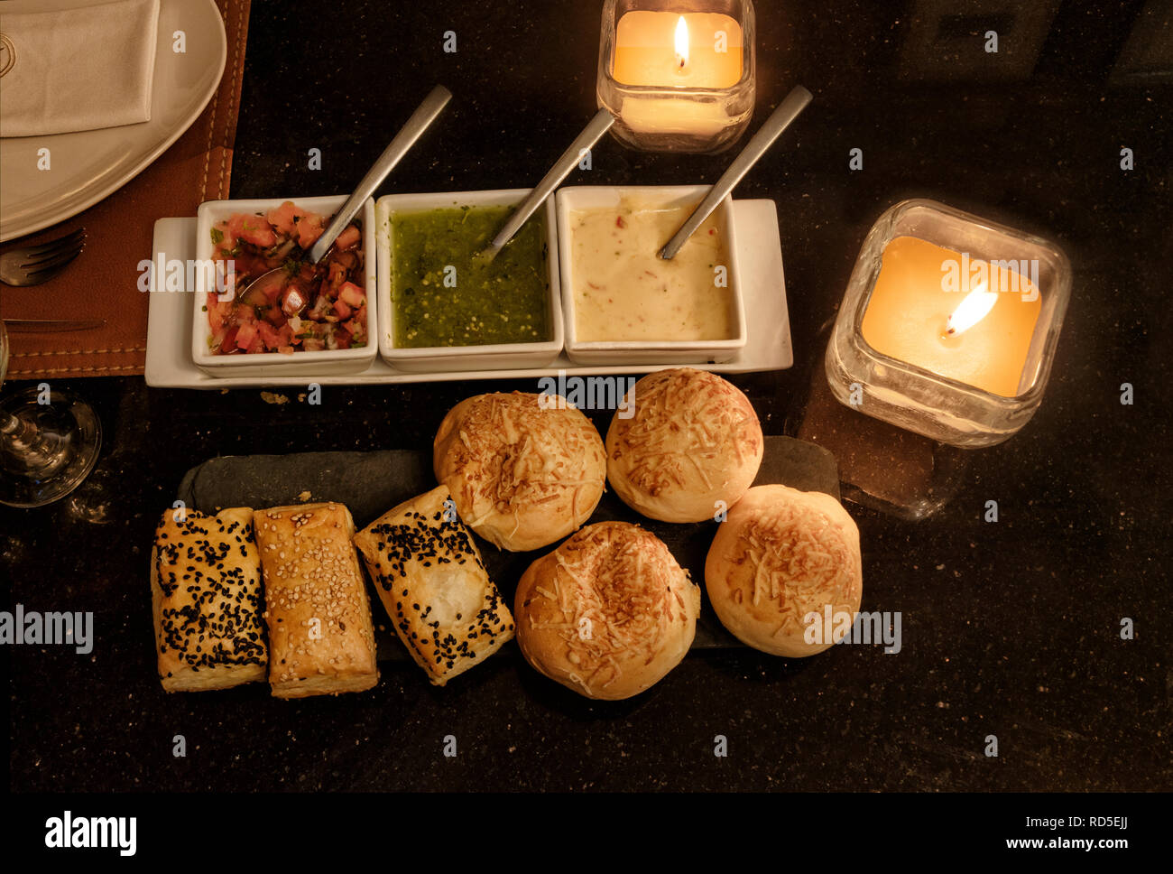 Many types of bread rolls and sauces, with candles on elegant black granite table top Stock Photo