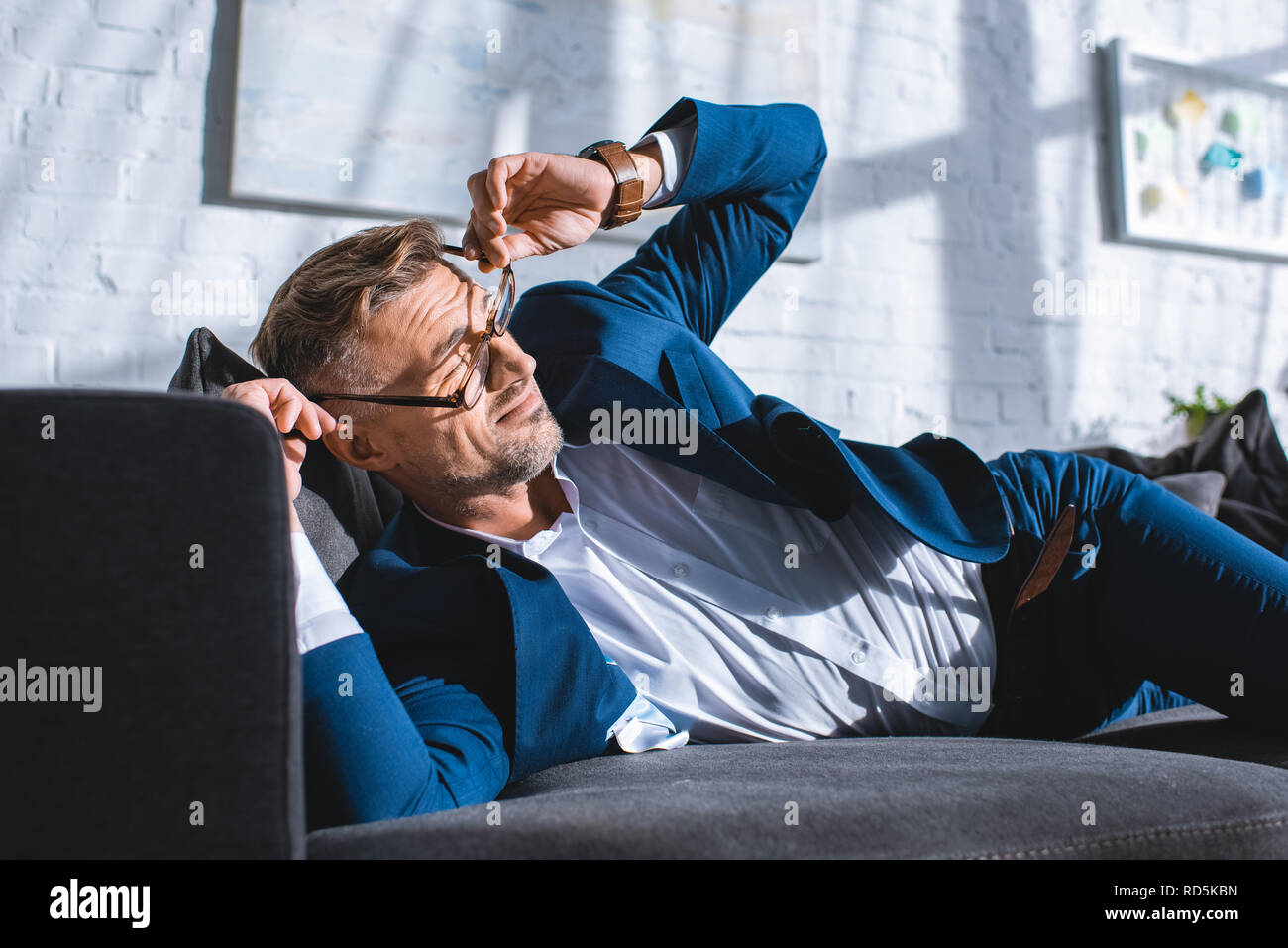 drunk businessman wearing glasses while lying on sofa Stock Photo