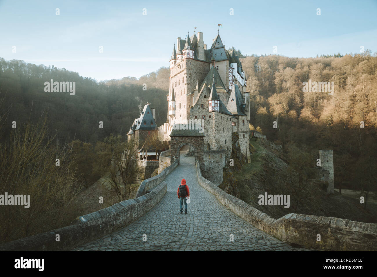 Panorama view of young explorer with backpack taking in the view at famous Eltz Castle at sunrise in fall, Rheinland-Pfalz, Germany Stock Photo