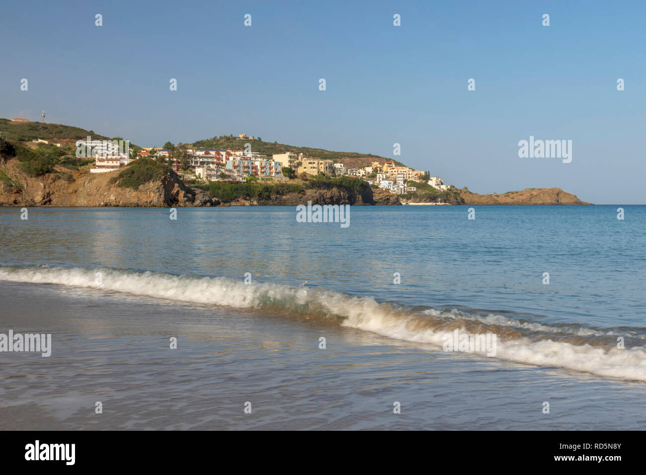 Wave comming in to a sandy beach and houses on the hill behind, picture from the Bali area in Rethymno on Crete Island. Stock Photo