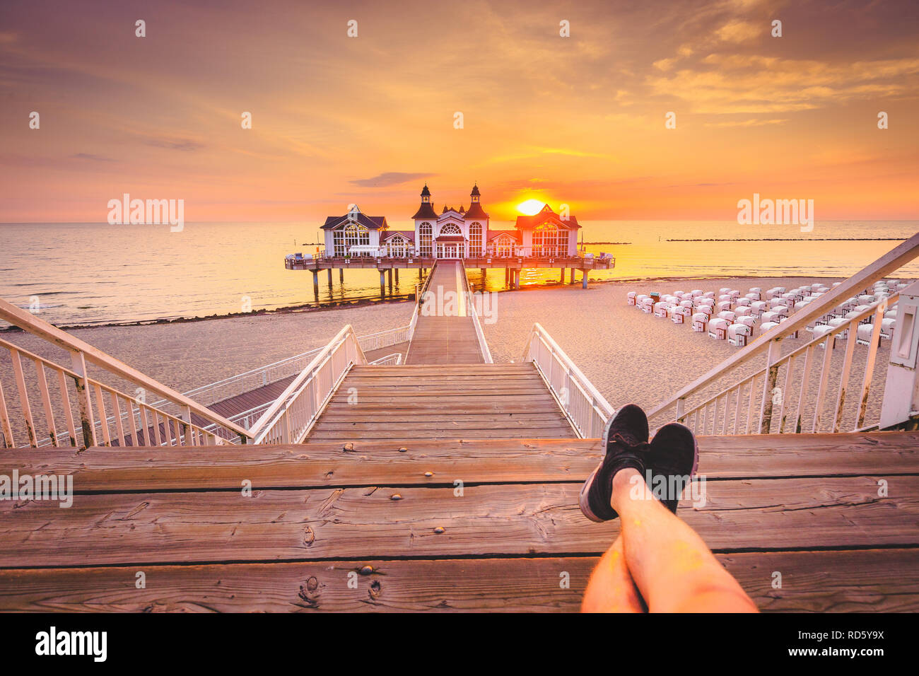 Young man sitting on wooden pier enjoying beautiful sunrise at famous Seebrucke Sellin at Ostseebad Sellin, island of Ruegen, Baltic Sea, Germany Stock Photo