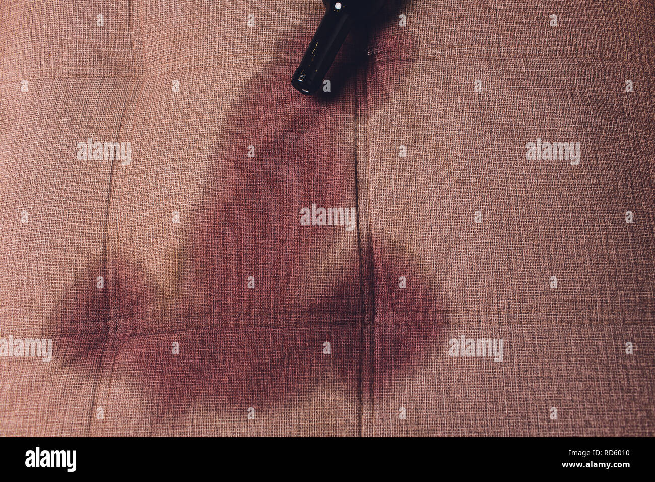 Red wine spilled on a brown couch sofa. dark bottle of red wine dropped