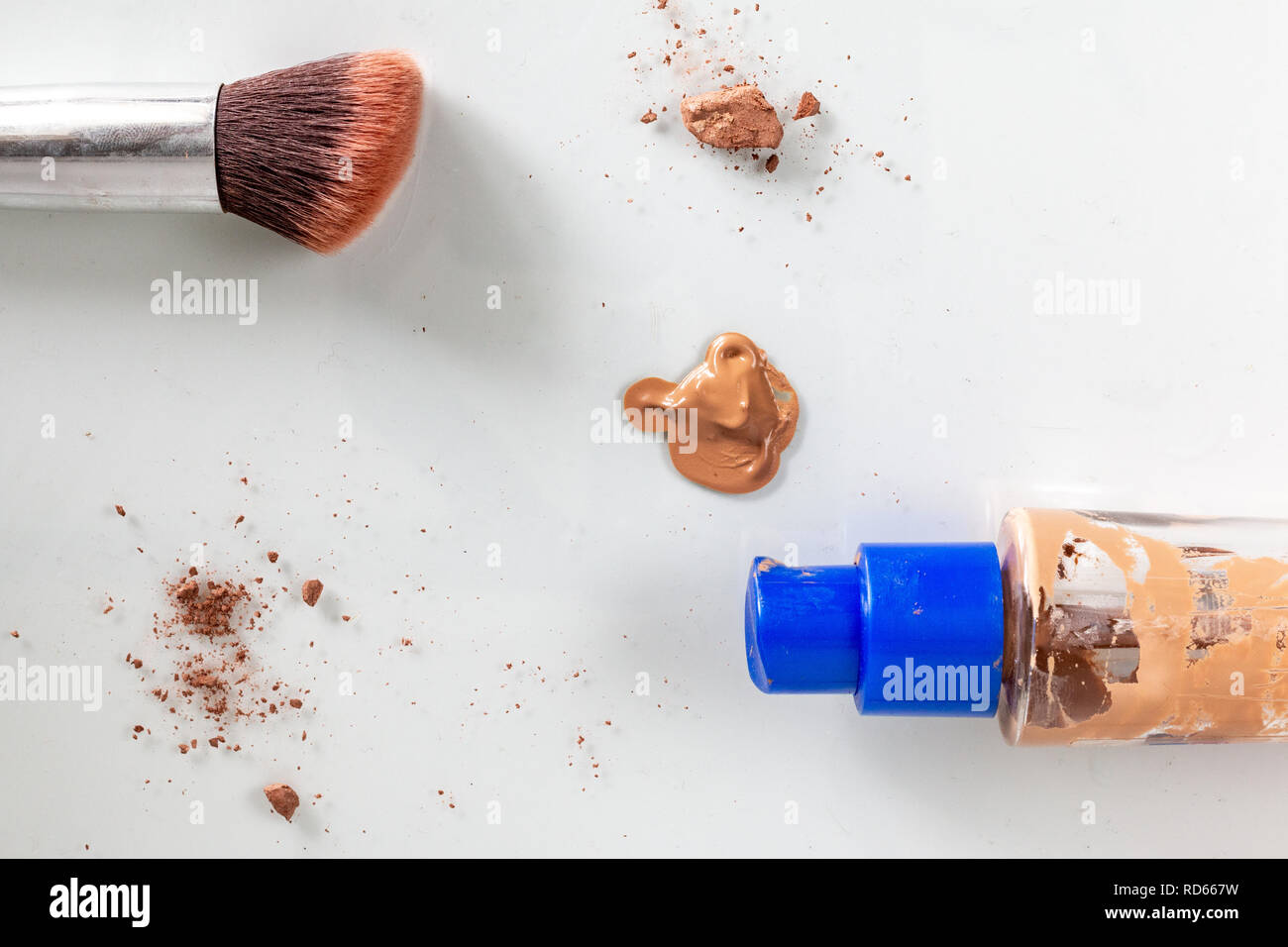 flat lay of makeup showing a makeup brush and glass bottle, surrounded by scattered makeup. Stock Photo