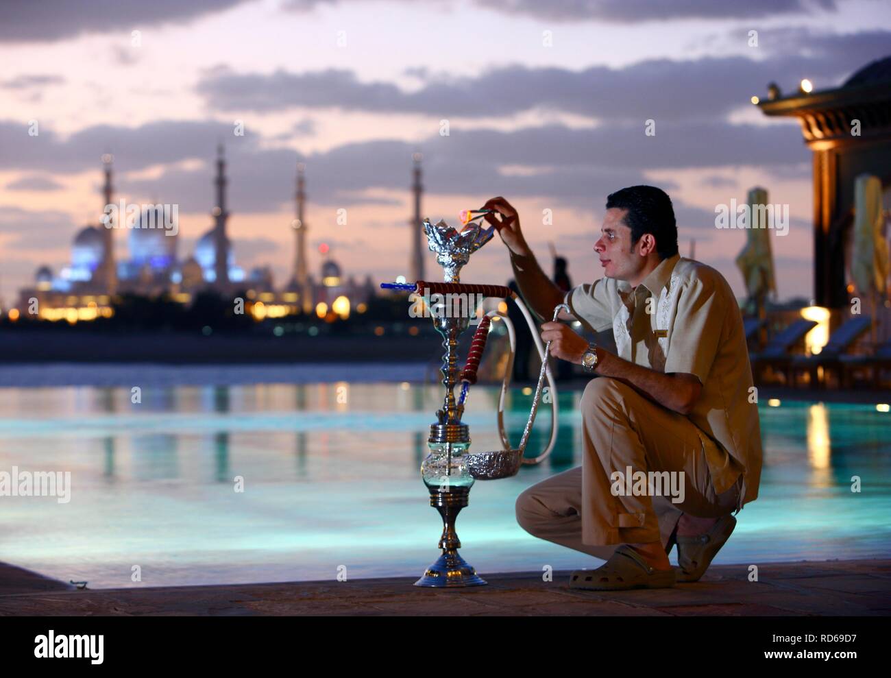 Man with hookah, water pipe, hotel pool, Shangri-La Hotel, Qaryat Al Beri, view on the Sheikh Zayed Mosque, Abu Dhabi Stock Photo