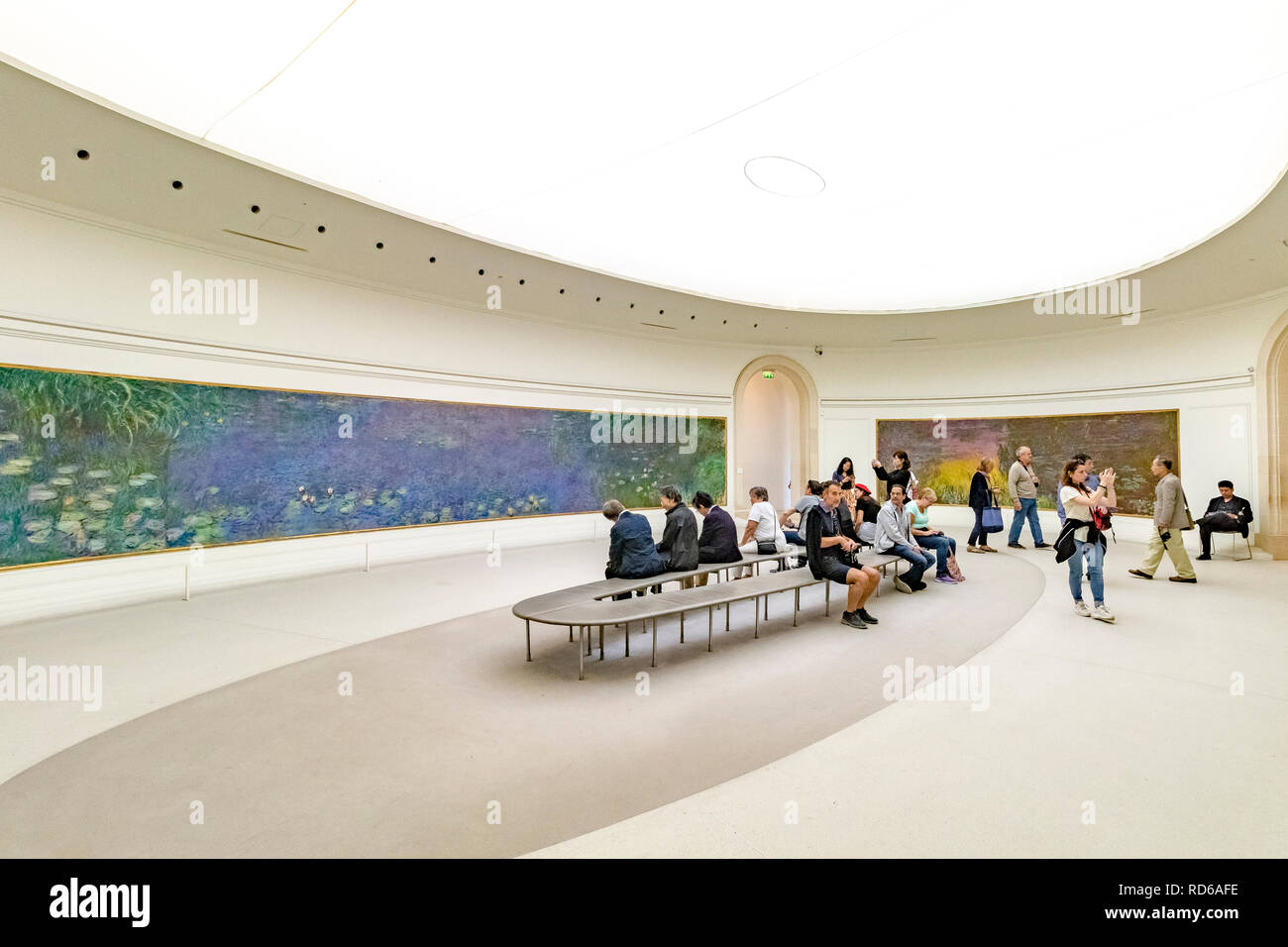 People looking at the Water Lilies by Claude Monet set in curved panels in an oval shaped room at The Orangerie or Musee de l'Orangerie ,Paris, France Stock Photo