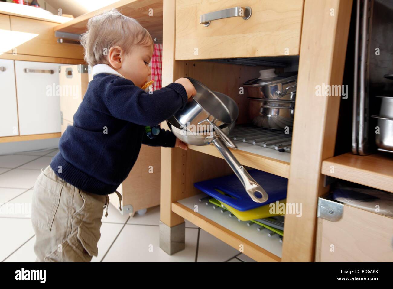 Little boy, 10 months, taking cooking pots from a cupboard in the
