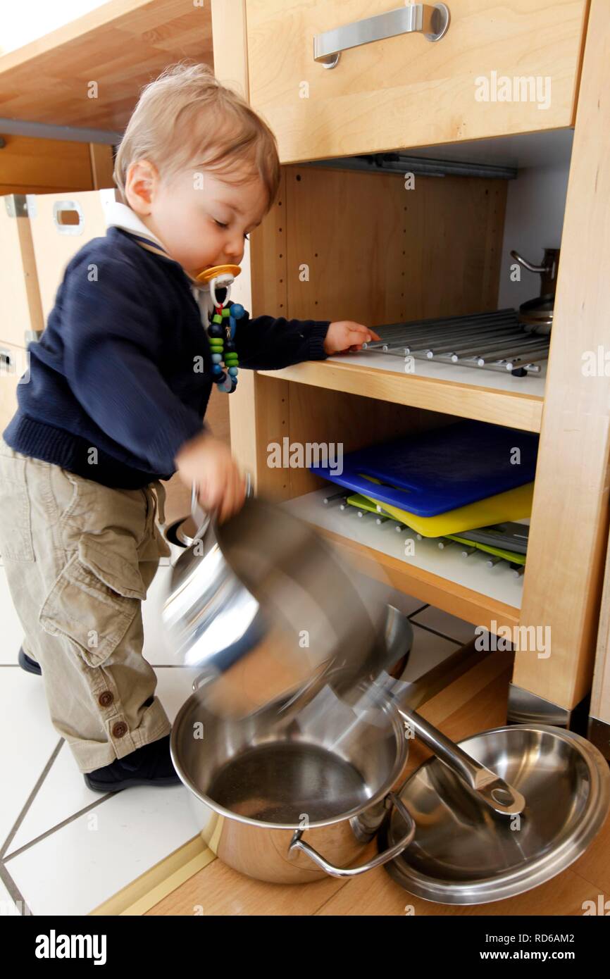 Little boy, 10 months, taking cooking pots from a cupboard in the