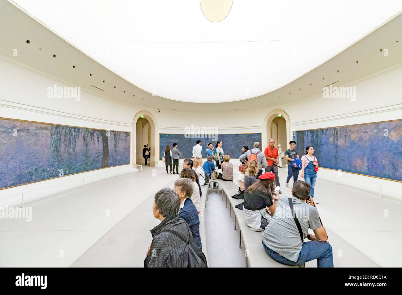 People looking at the Water Lilies by Claude Monet set in curved panels in an oval shaped room at The Orangerie or Musee de l'Orangerie ,Paris, France Stock Photo