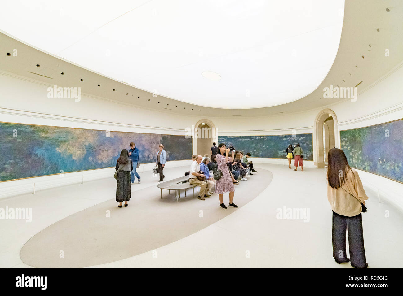 People looking at the Water Lilies by Claude Monet set in curved panels in an oval shaped room at The Orangerie or Musee de l'Orangerie ,Paris, France Stock Photo