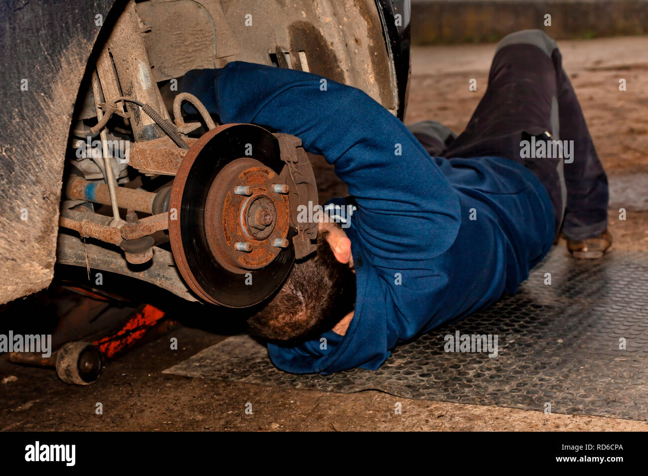 A mechanic works lying on the ground repairing an old car Stock Photo