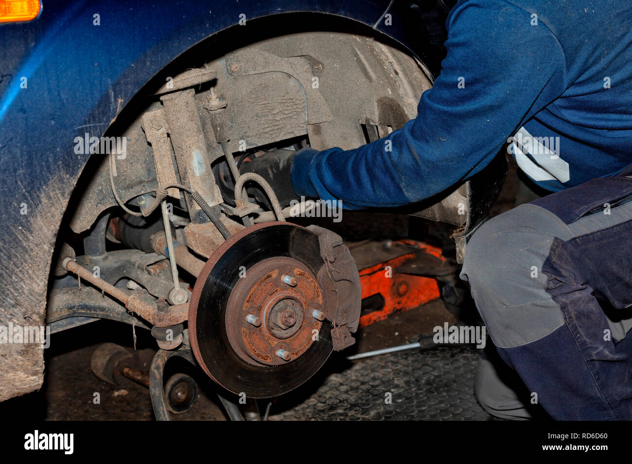 A mechanic works on his knees on the ground repairing an old car Stock