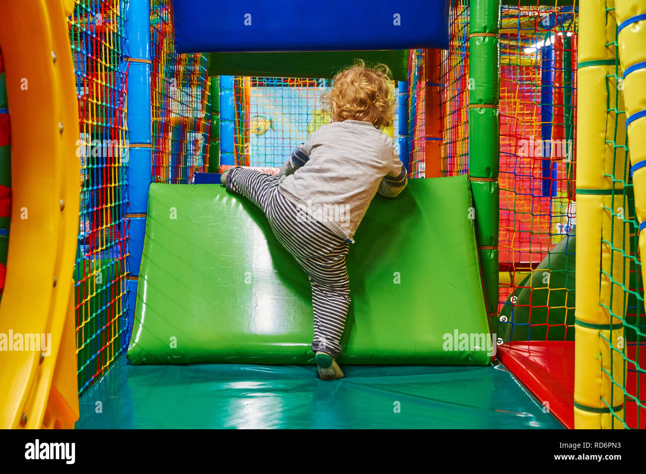 Child trying to climb over an obstacle on a softplay frame showing determination and perseverance. Stock Photo