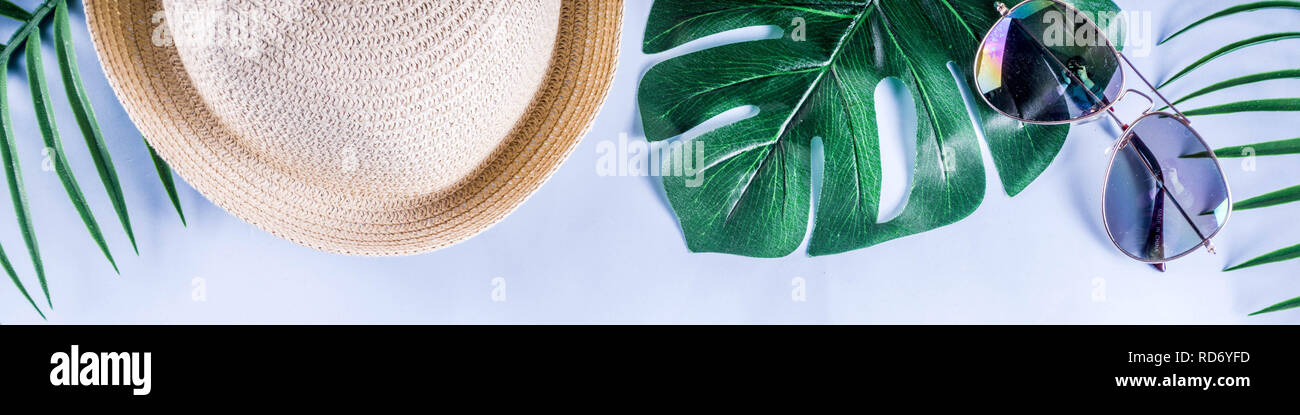 Colorful summer vacation and holiday flat-lay. Straw hat, sunglasses, palm and monstera leaves on bright blue yellow background, top view, copy space  Stock Photo