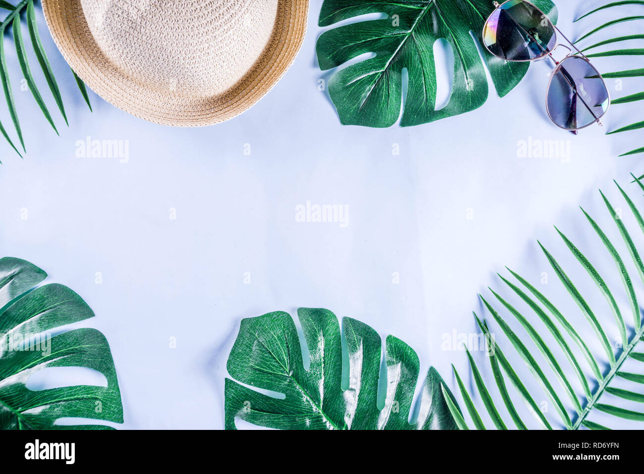 Colorful summer vacation and holiday flat-lay. Straw hat, sunglasses, palm and monstera leaves on bright blue yellow background, top view, copy space Stock Photo