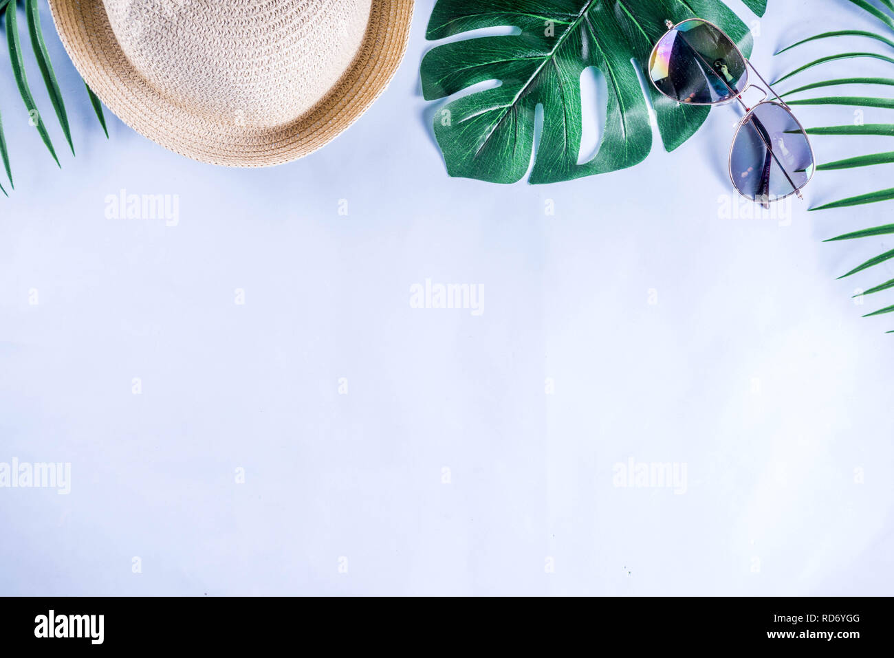 Colorful summer vacation and holiday flat-lay. Straw hat, sunglasses, palm and monstera leaves on bright blue yellow background, top view, copy space Stock Photo