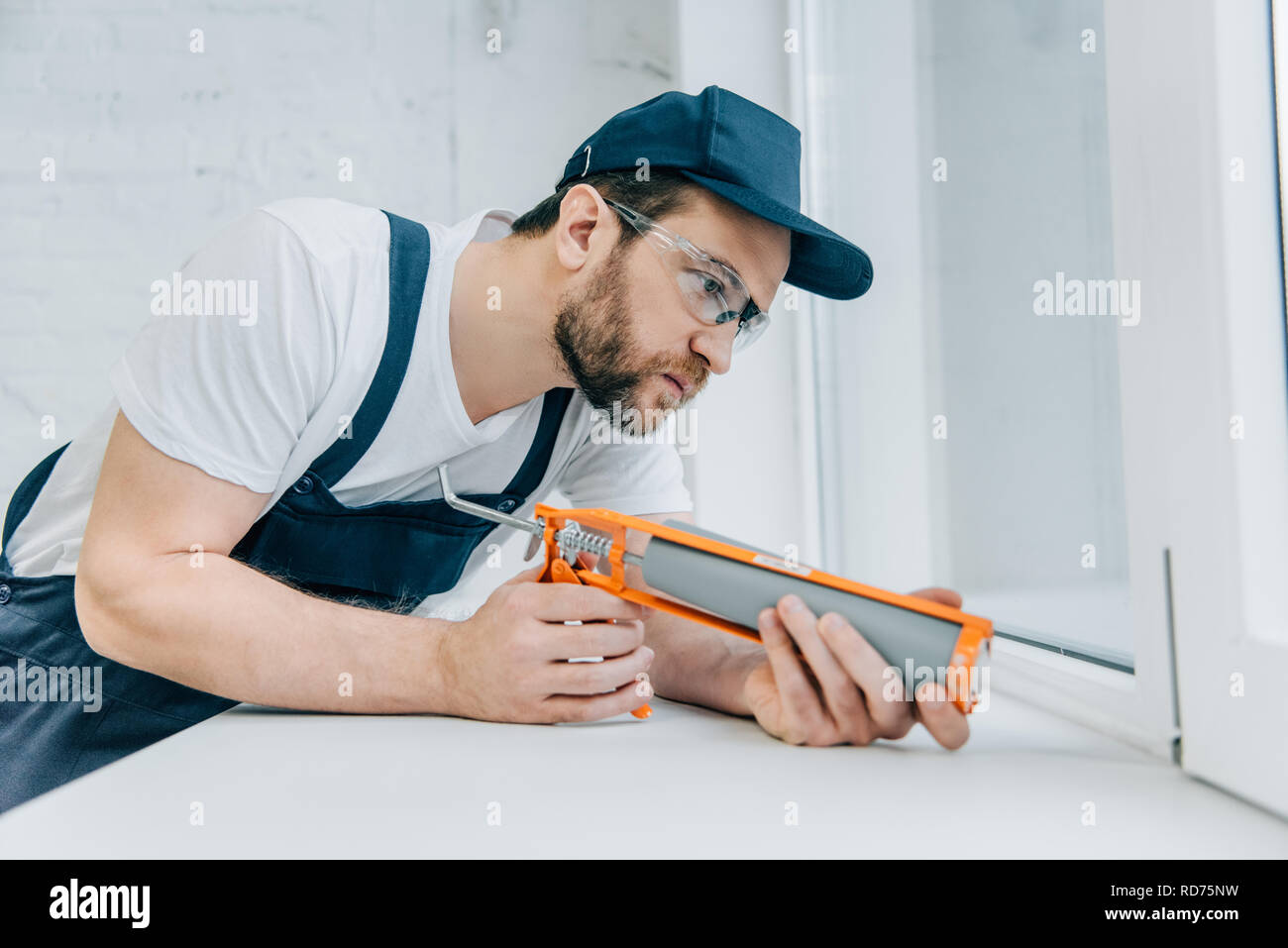 concentrated adult repairman fixing window with sealant gun Stock Photo ...