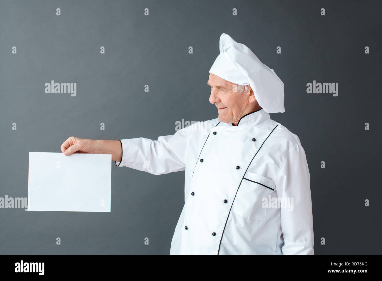 Senior chef studio standing isolated on gray looking at paper curious Stock Photo