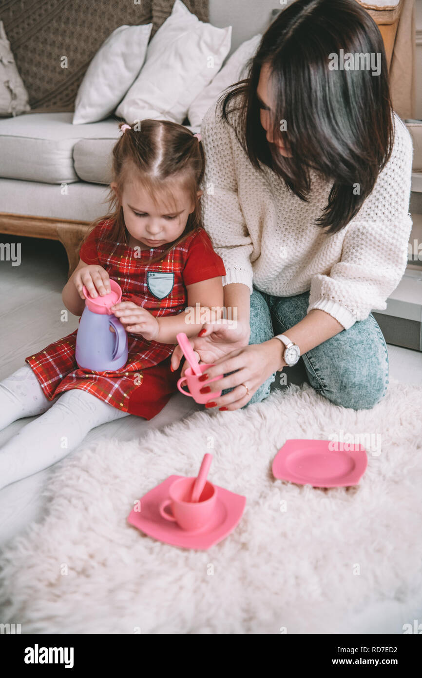 Happy loving family. Mother and her daughter girl play tea-party and drink tea from cups in children room. Funny mom and lovely child having fun indoors Stock Photo