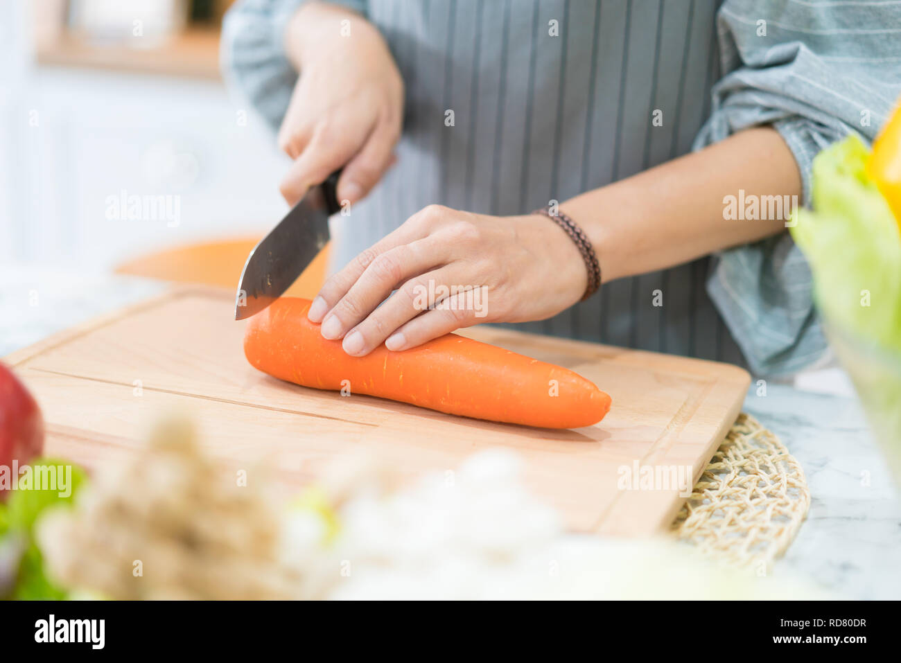 Hand with knife cutting carrot. Woman prepares food at table. Chef cooks delicious dinner. Work that requires skill. Stock Photo