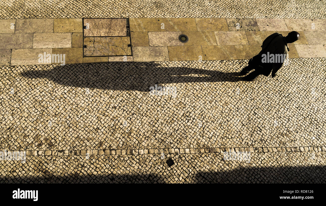 Lisbon, Portugal. Man with a long shadow walking down Rua Barros Queirós near Rossio square in the afternoon light. Typical limestone pavement. Stock Photo