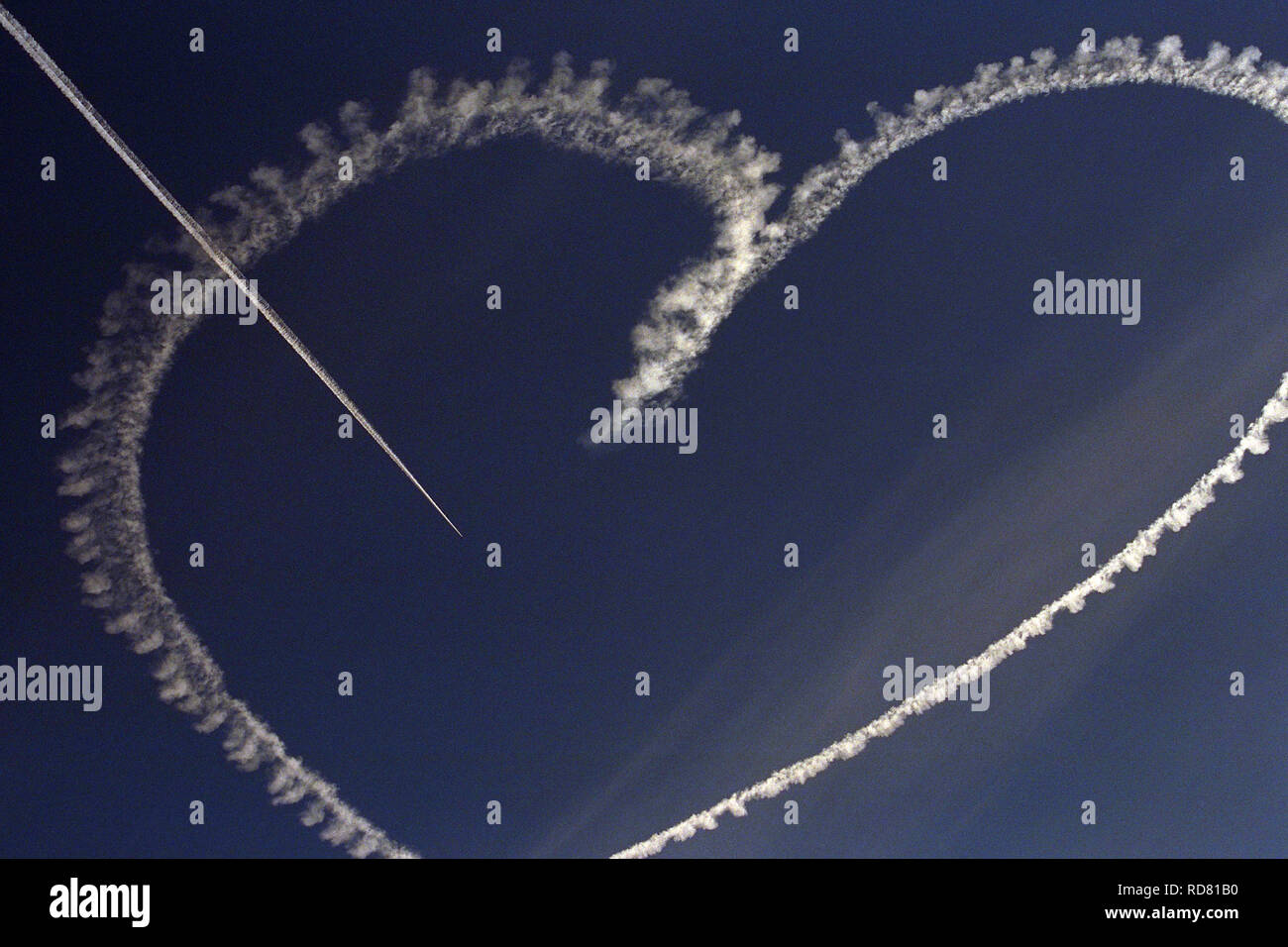 Using paraffin oil in the exhaust a small airplane does a skywriting skydrawing heart and finishes with an arrow piercing through it. Stock Photo