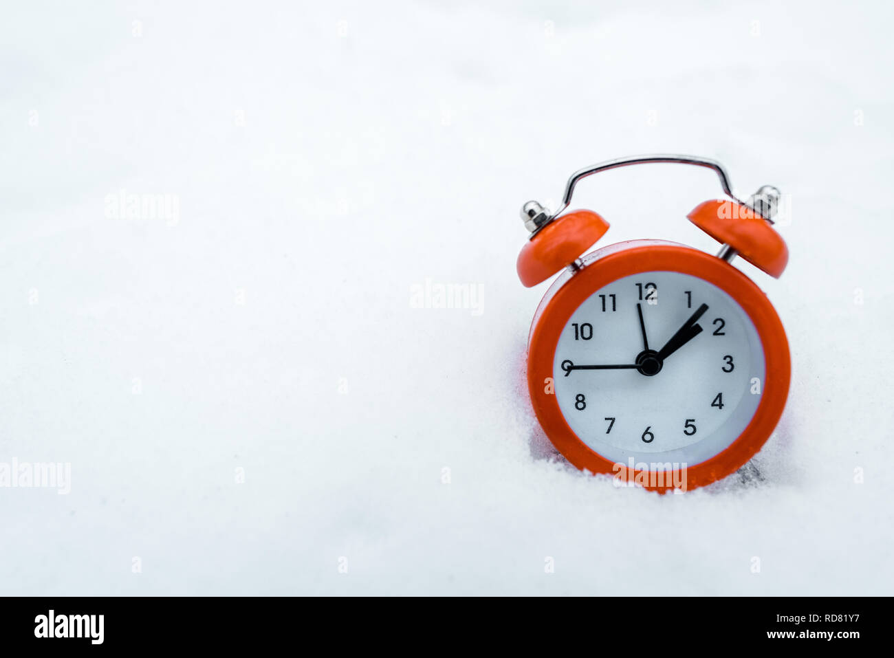 red retro alarm clock standing on white snow near trees in snowy forest Stock Photo