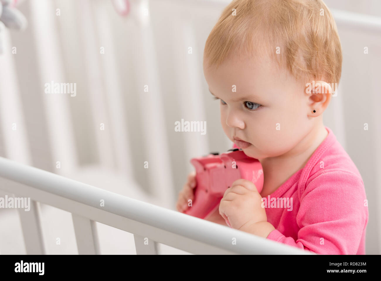Adorable Kid In Pink Shirt Holding Pink Joystick In Crib And