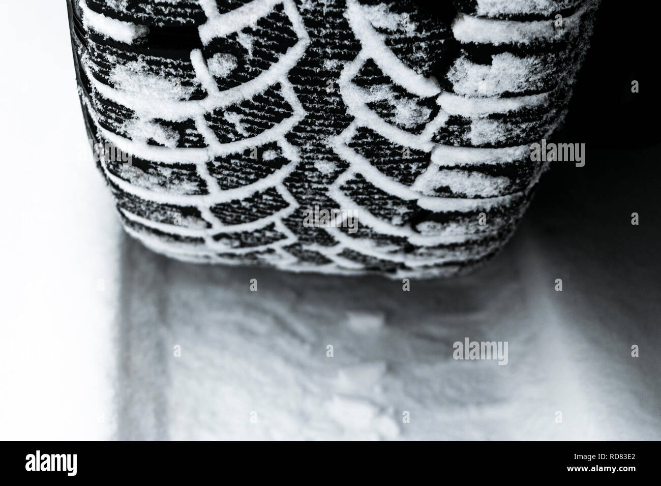 The car tire in the snow close up. Car tracks on the snow. Traces of the car in the snow. Winter tires. Tyres covered with snow at winter road. Stock Photo