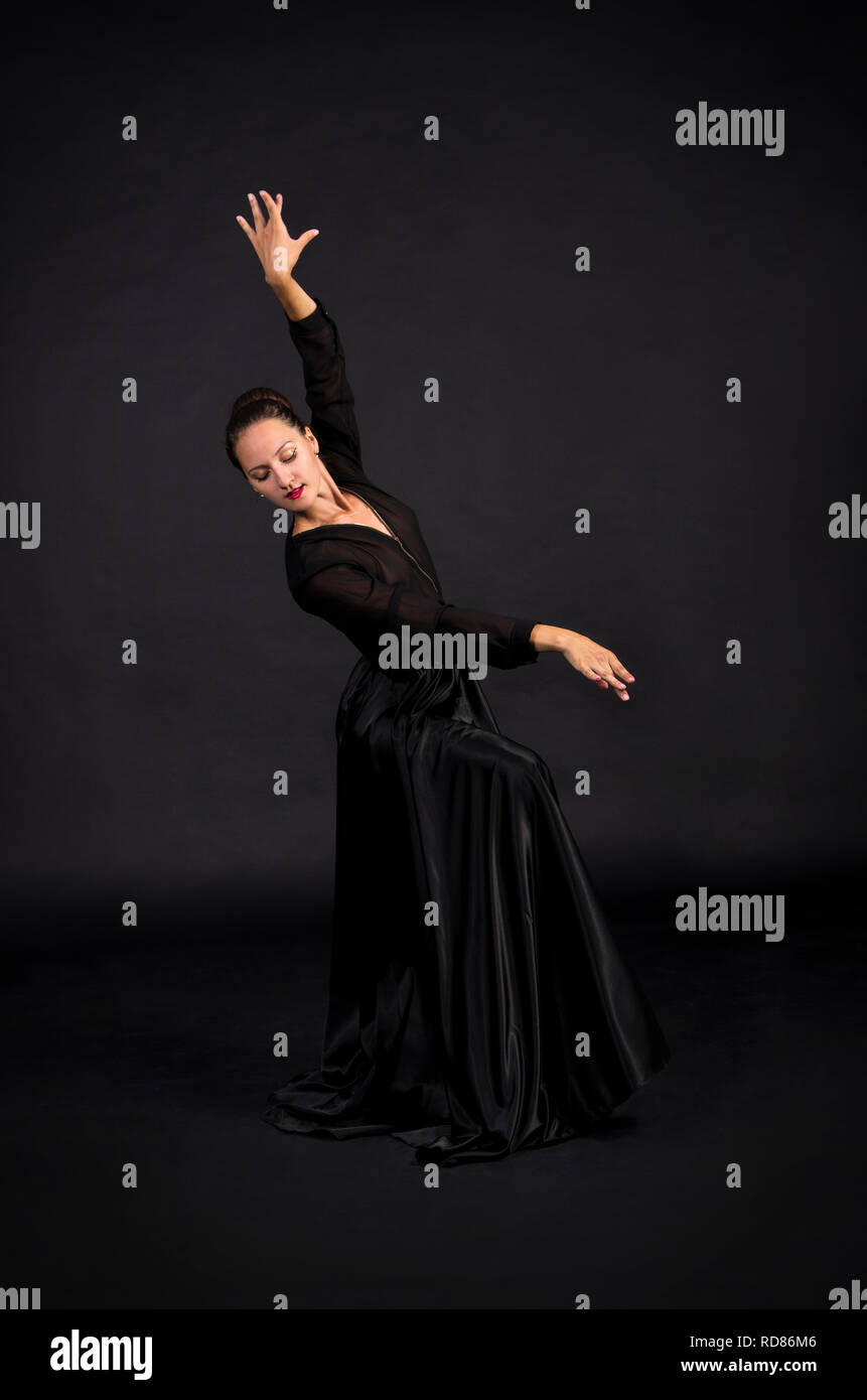 A Young, smiling woman in black suit dancing modern choreography.Studio shot on dark background, isolated image. Stock Photo